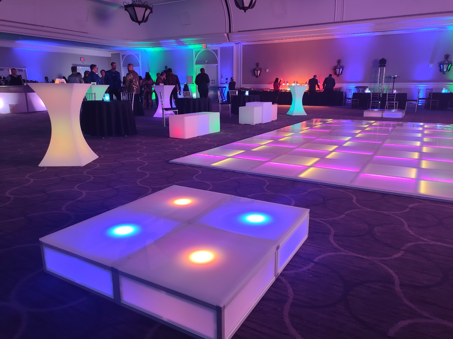 Illuminated dance platforms glowing in a ballroom beside a lit LED dance floor