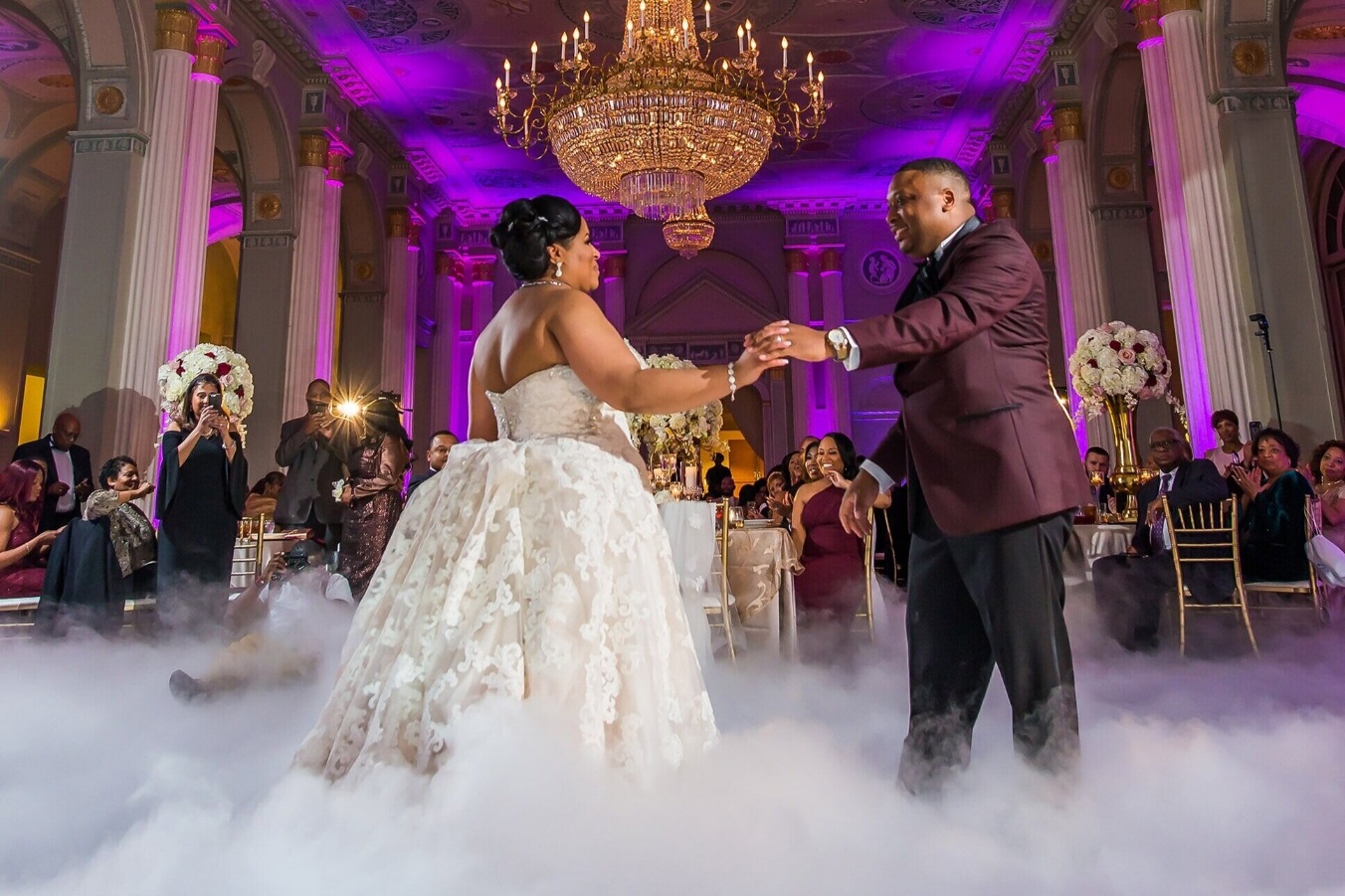 Couple dancing in a low, thick cloud under a crystal chandelier in a purple-lit ballroom