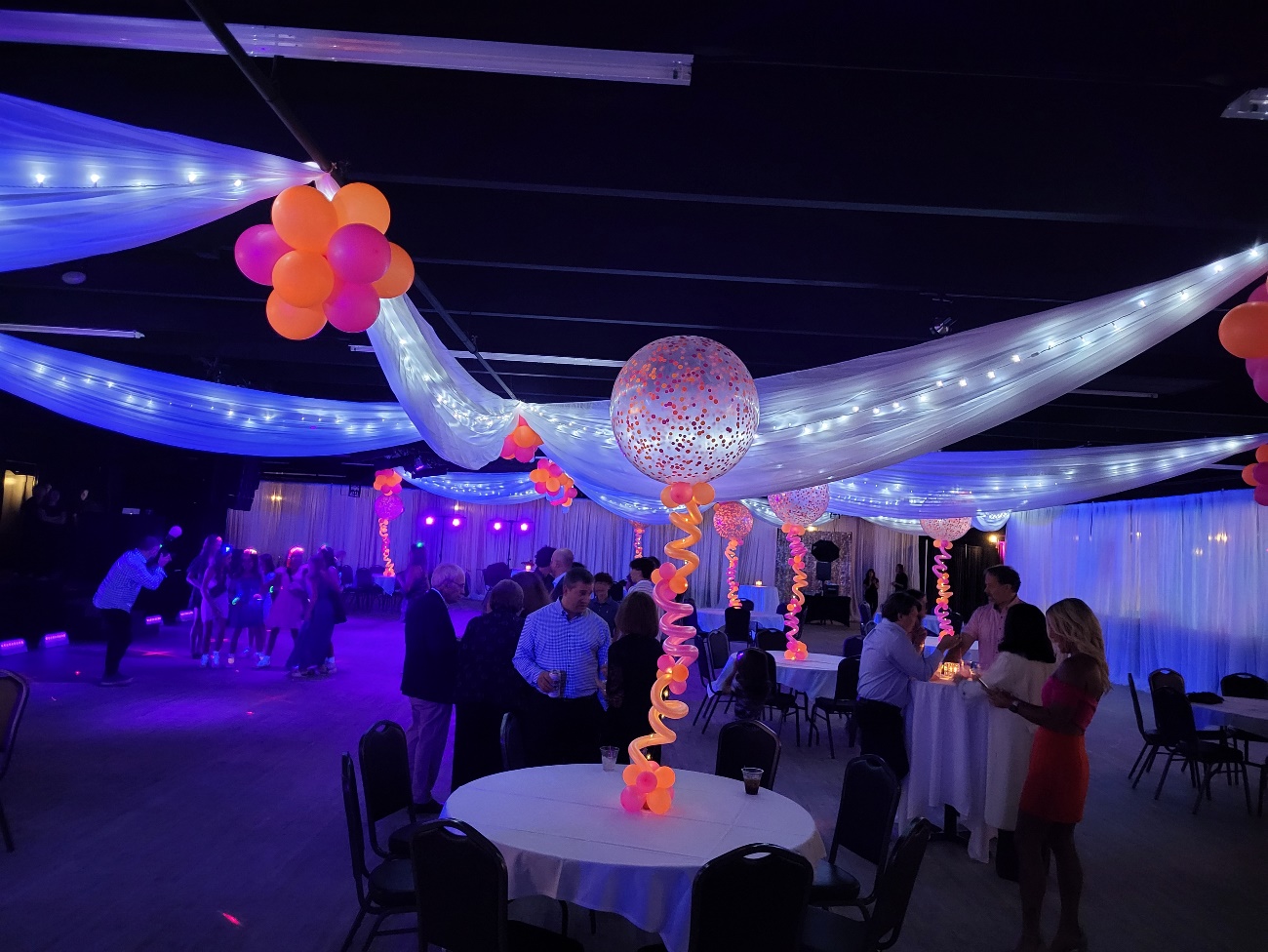 Room under blacklight with neon balloon columns and glowing ceiling drapes