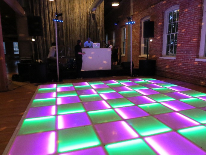 Green and pink LED dance floor in front of the DJ booth in a brick-walled venue