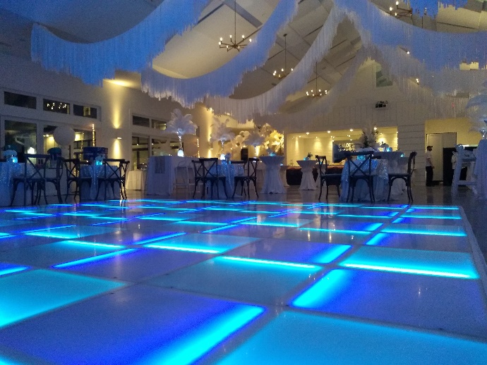 Blue LED dance floor in a white ballroom with feather centerpieces and a draped ceiling
