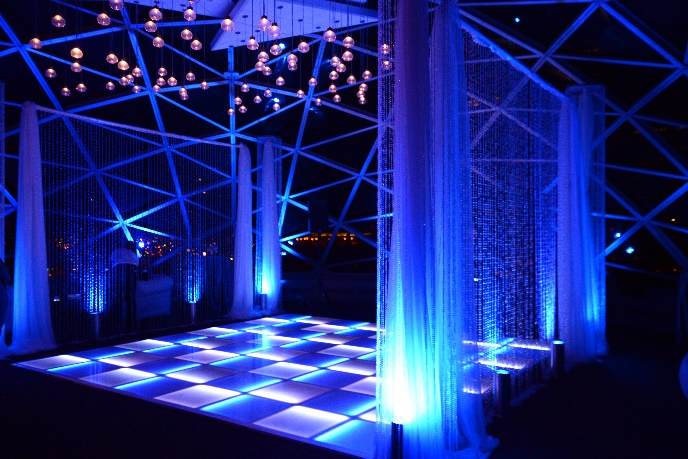 Blue LED dance floor under a geometric frame hung with crystal strands and glowing globe lights